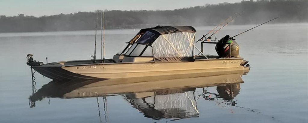 Billy's aluminum fishing boat with a canopy and rods rigged, sitting on a still lake in the morning mist.
